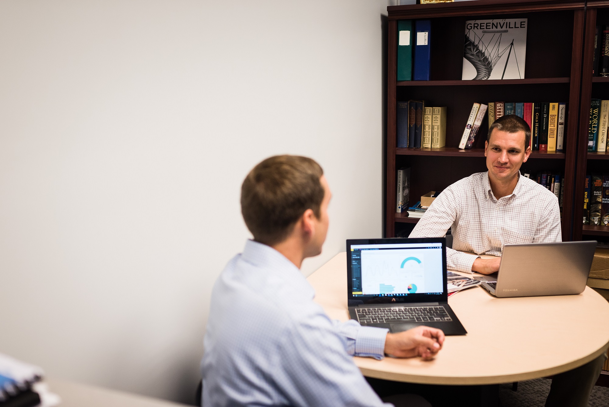 Guys talking at table with computer with Internet of Things dashboard displayed