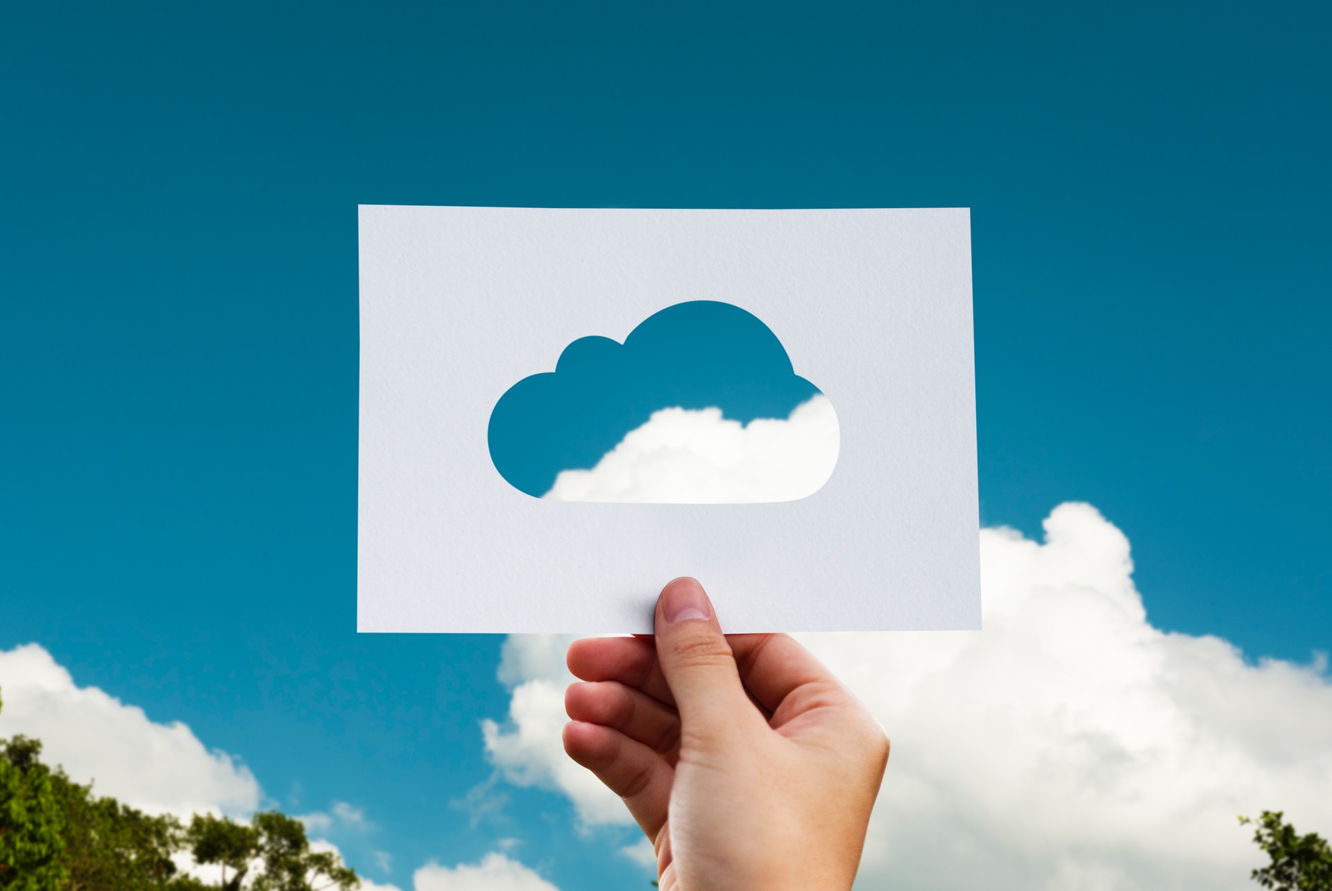 Blue sky with hand holding a paper cut-out of a cloud