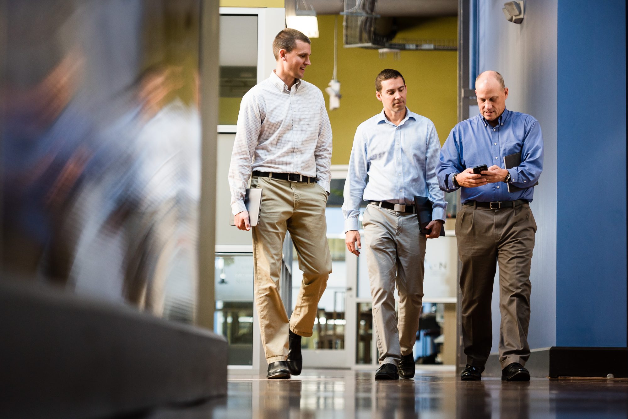 Three men walking down hallway looking at a phone