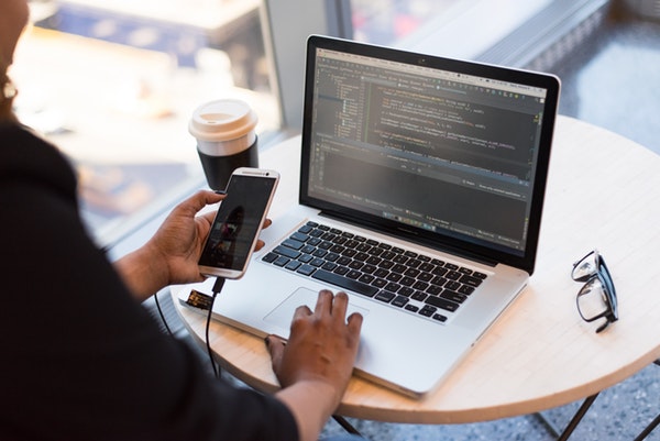 Woman holding phone and looking at macbook with code on screen