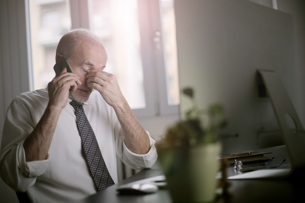 businessman rubbing eyes while talking on a smartphone