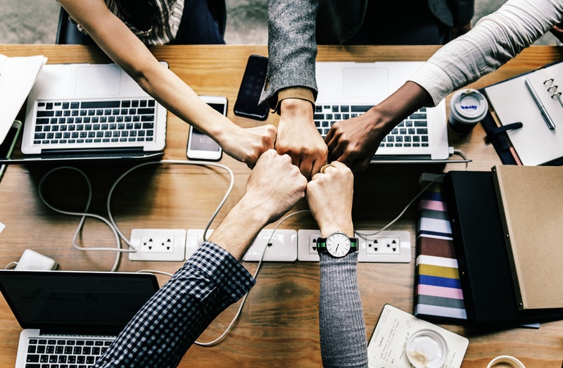 Colleagues giving each other a fist bump with computers below their hands