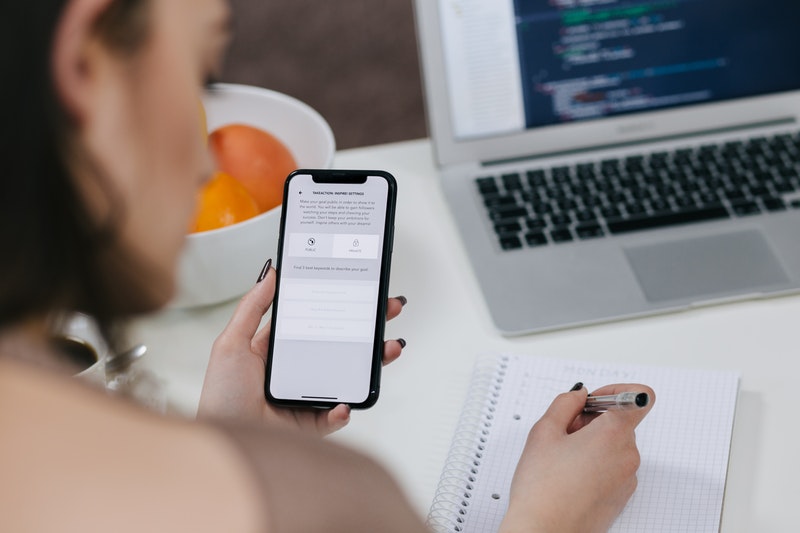 Woman looking at phone and writing on notepad