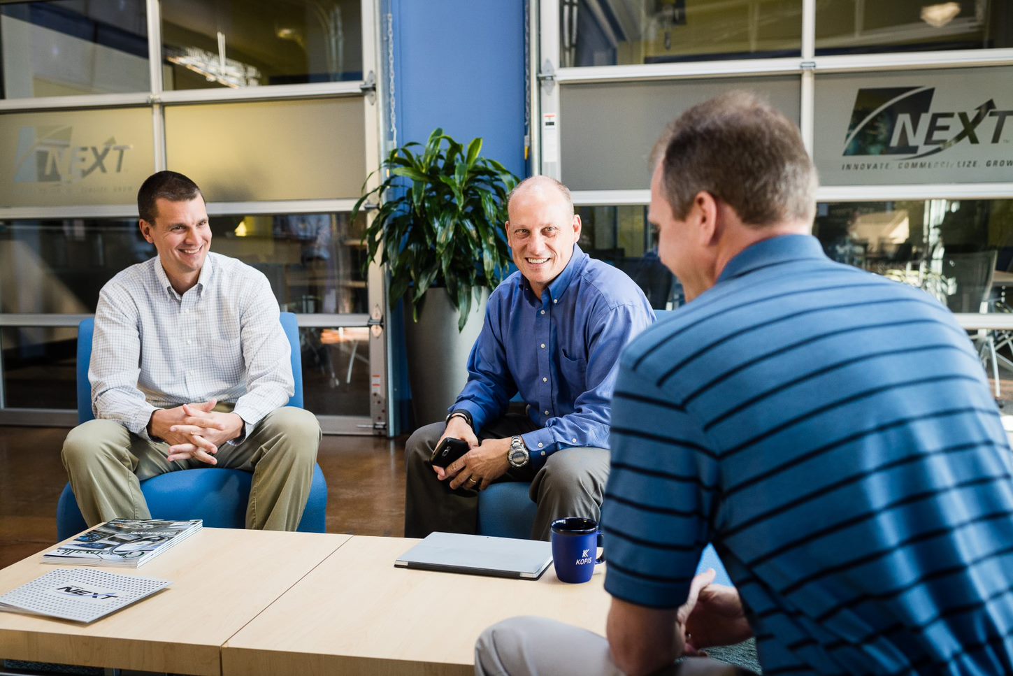 Three men smiling and talking at a desk