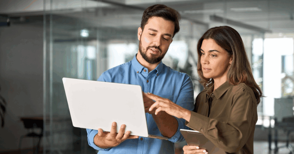 Two business professionals reviewing data on a laptop in a modern office, discussing insights powered by advanced analytics for better decision-making.